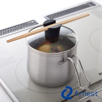 不鏽鋼料理鍋，附玻璃鍋蓋，鍋蓋上放置一雙木筷。鍋身為銀色不鏽鋼材質，有一個金屬提把。鍋內可見食物。