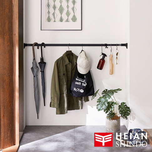 黑色伸縮桿上懸掛著兩把雨傘、一件軍綠色外套、一頂白色帽子、一個黑色帆布袋、一個棕色噴瓶、一把木柄刷和一串鑰匙。