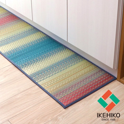 藺草編織的長方形地墊，帶有藍、黃、紅、綠等多色橫向條紋，邊緣為深藍色滾邊，置於淺木紋地板上，旁有白色櫥櫃。
