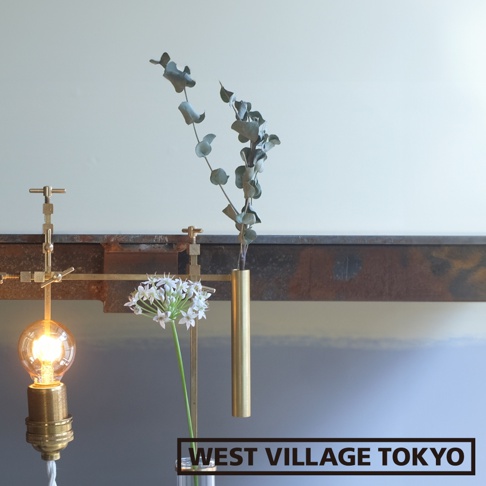 黃銅可夾式金屬花器，展示了帶有燈泡的工業風燈座，和一個細長的黃銅花瓶，瓶中插有綠葉植物，旁邊還有白色小花。