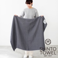 一位女士展示著一條深灰色、2.5層紗材質的浴巾，浴巾呈現自然的皺褶紋理，左上角有一個白色標籤，右下角有「SHINTO TOWEL EST. 1907」字樣及品牌標誌。