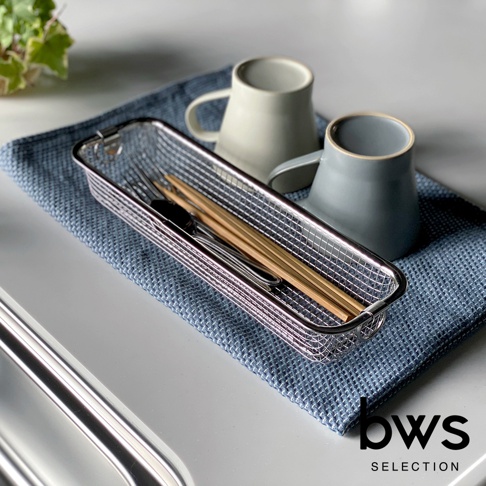 不鏽鋼長型簡約瀝水籃，內部裝有木筷子、叉子和湯匙。籃子放在藍色紋理布上，背景有兩個淺灰色和深灰色的馬克杯。