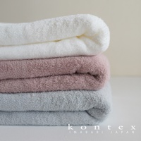 堆疊的浴巾，由上至下分別為白色、粉紅色和淺灰色，質地蓬鬆柔軟。