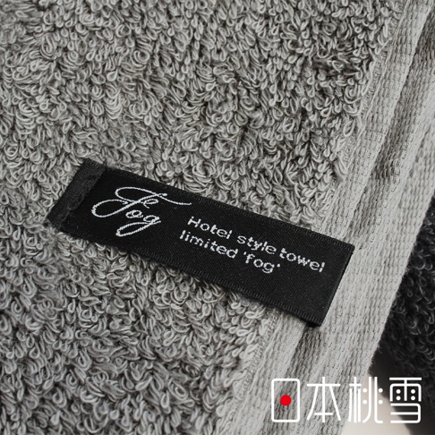 一塊灰色厚實的毛圈毛巾，帶有黑色標籤，上面印有「fog」標誌和「Hotel style towel limited 'fog'」字樣。