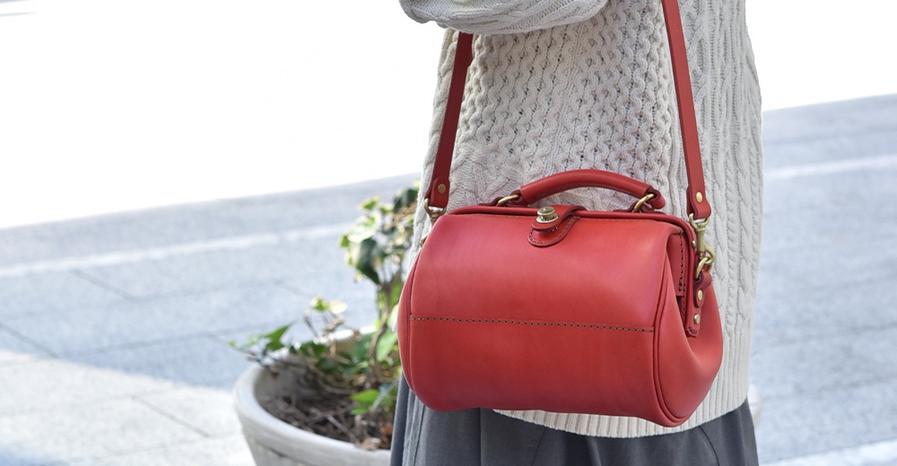 紅色皮革口金醫生單肩包，配有頂部提把和可拆卸肩帶，金色金屬扣環，縫線細緻。