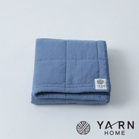 藍色格紋鋪棉毛巾，材質觸感柔軟，邊緣有細緻包邊，角落處有白色品牌標籤。