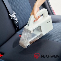 手持白色 Iris Ohyama 無線織物清潔機，正在清潔汽車座椅的黑色和藍色織物表面。