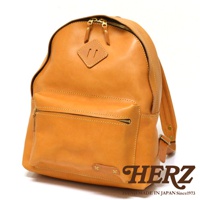 職人手作皮革休閒風後背包，採用鞣製皮革製成，呈現自然棕色調。包款正面設有拉鍊式收納袋，頂部有雙拉鍊設計，並點綴菱形皮革飾片。整體風格簡約，適合日常休閒穿著。