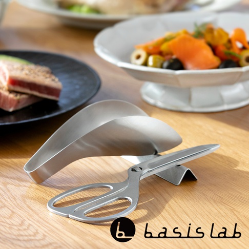 一體成形的不鏽鋼料理剪刀，剪刀部分呈現銀色金屬光澤，刀刃為鋒利狀，手柄部分有鏤空設計，剪刀可拆分成兩部分，放置於木質桌面，背景有餐盤和食物。