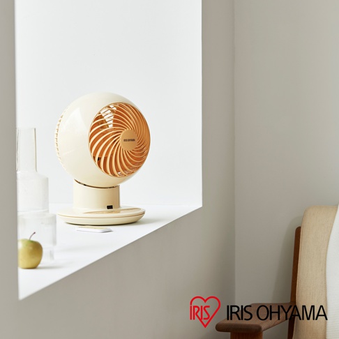 一台米白色球形空氣循環扇，扇葉為橘色，擺放在窗台邊，旁邊有綠色小蘋果和透明玻璃瓶，下方有遙控器。