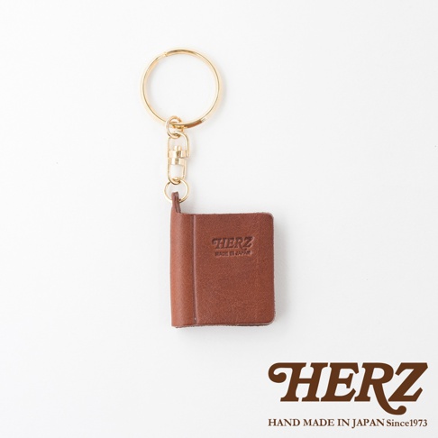 職人手作皮革書本造型鑰匙圈，採用棕色皮革製成，小巧的書本造型，上面壓印有「HERZ」與「MADE IN JAPAN」字樣，搭配金色金屬鑰匙圈。