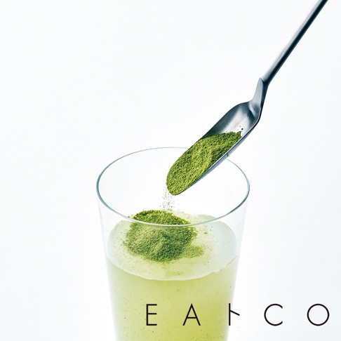 銀色金屬製的小長勺，正將綠色粉末舀入裝有淺綠色飲品的透明玻璃杯中。