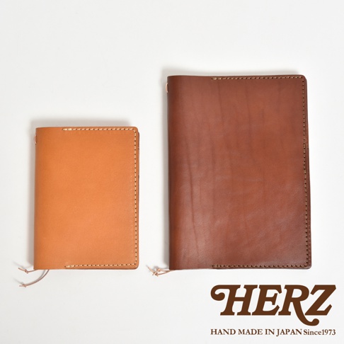 兩個手工皮革手帳書套，一個為淺棕色，另一個為深棕色，並印有HERZ品牌標誌。