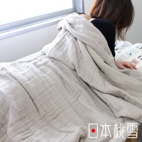 一層淺米色八層紗透氣被，質感柔軟，表面有自然的皺褶紋理，覆蓋在一名正在閱讀的女子身上，背景為窗戶和床鋪。