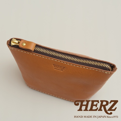 職人手作皮革三角收納包，棕色牛皮材質，配有金色拉鍊與皮革拉頭，縫線清晰，品牌壓印於包面上。
