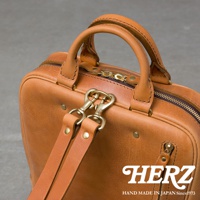 HERZ 品牌標誌，下方印有 HAND MADE IN JAPAN Since1973，整體為棕色皮革後背包的局部特寫，展現其精緻工藝與材質。