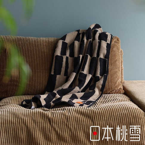 日本桃雪户外格纹棉柔迷你浴巾，带有标志性的格子图案，搭在条纹纹理的棕色沙发上。