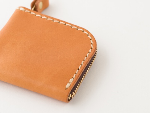 淺棕色皮革零錢包，帶有米白色縫線和金色拉鍊，包角處有皮革掛環。