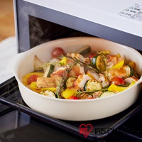 淺米色陶瓷不沾平底鍋中盛有烤雞肉、櫛瓜、番茄、黃甜椒與迷迭香，鍋子放在烤箱架上，散發熱氣。