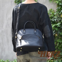 黑色皮革貝殼手提包，設有金色拉鍊和金屬腳釘，可肩背或手提。