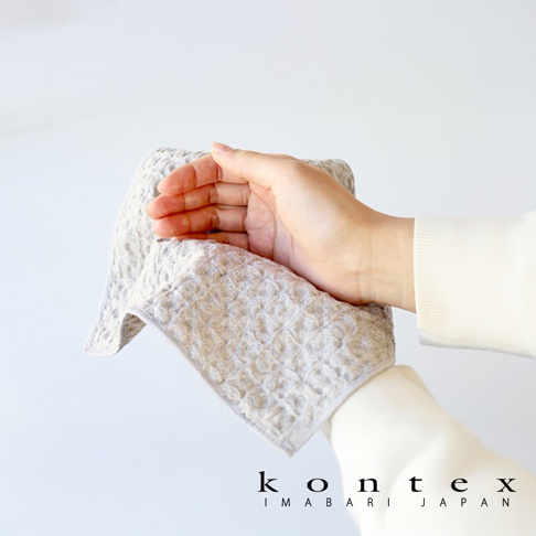 一隻手拿著一塊淺灰色的棉麻混紡方巾，方巾表面有蜂窩狀的鬆餅紋理，邊緣縫有灰色線。