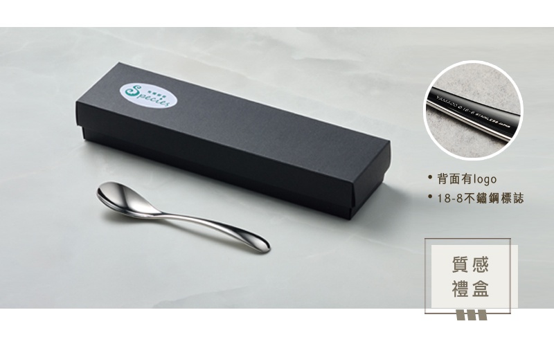 精緻的黑色禮盒旁擺放著一把閃亮的銀色不鏽鋼點心匙，匙柄上印有品牌標誌及18-8不鏽鋼標記。