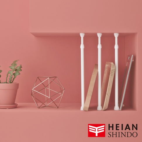 展示架上，三個白色兩段式強化伸縮桿，下方擺放著兩個木製隔板和一個鏡面物品。左側有盆栽綠植及金屬幾何裝飾。