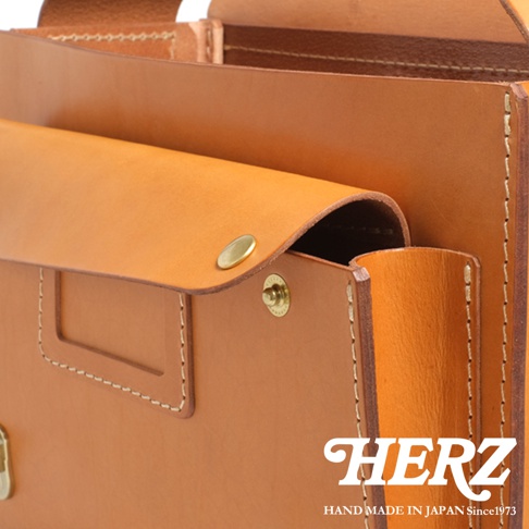 HERZ 手工皮革包，近拍展示其精緻縫線與金屬扣細節，品牌標誌與手工製造字樣清晰可見