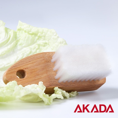 赤田AKADA 品牌字樣搭配木柄纖維刷與新鮮白菜葉的靜物照