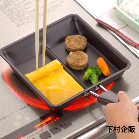 深灰色二合一分格平底鍋，鍋內有剛煎好的蛋捲、兩塊肉餅、一塊花椰菜和一小段紅蘿蔔。