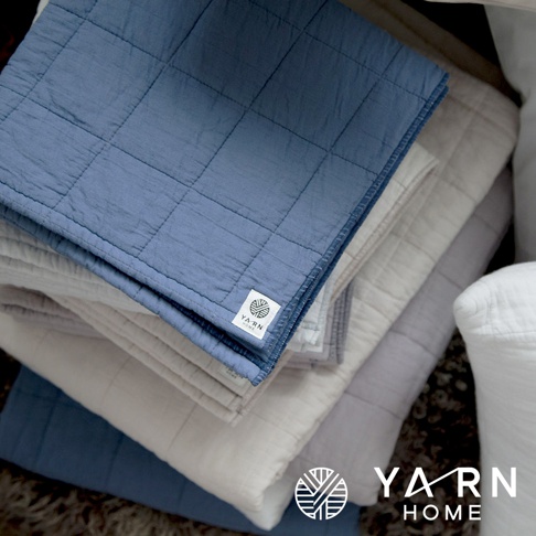 一疊UKIHA脫脂棉混紗速乾格紋浴巾，顏色包含藍色、米色、淺紫色和白色。浴巾表面有壓紋格紋，邊緣有細緻的縫線。其中一條藍色浴巾上，可見「YARN HOME」品牌標籤。