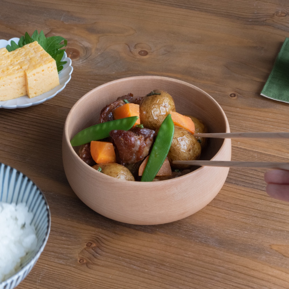 淺色楓木沙拉碗，盛有燉煮的馬鈴薯、胡蘿蔔塊、肉塊和豌豆，碗旁有筷子正在夾取食物，背景為木質桌面。