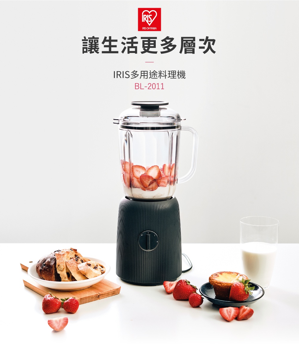 黑色條紋機身的果汁機，玻璃果汁壺內裝有草莓與白色液體，旁有裝有麵包的盤子、草莓和一杯牛奶。