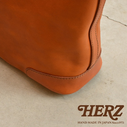 HERZ LOGO，HAND MADE IN JAPAN Since1973。橘色皮革托特包的底部細節，展現職人手工縫線。