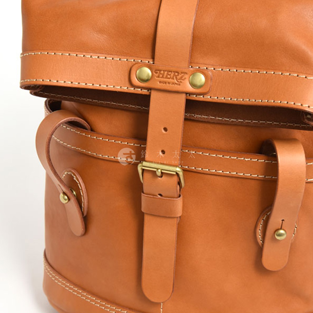 職人手作皮革雙口袋折蓋後背包，呈現自然皮革色澤，搭配金屬釦具與白色縫線，質感精緻。