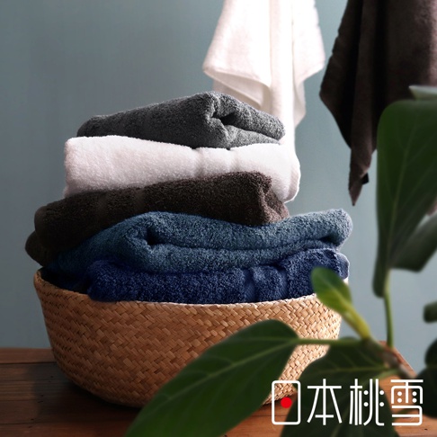 一籃堆疊的毛巾，包含深藍、藍綠、深棕、白色和深灰色，皆為蓬鬆柔軟的純棉材質。