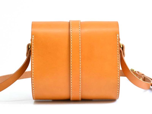 職人手作皮革皮扣單肩包 (CP-38)，採用天然棕色皮革製作，包身線條簡潔，正面中央有一條垂直皮帶和皮扣設計，邊緣縫線清晰，搭配可調節的皮革肩帶。