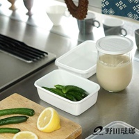 兩個白色長方型琺瑯保存容器，一個裝有小黃瓜，另一個是空的。旁邊有一個裝有乳白色液體的玻璃罐，蓋子為白色。