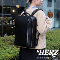 黑色皮革商務電腦後背包，具有方形輪廓、頂部提把、兩個拉鍊前袋和可調節肩帶，由職人手工製作。