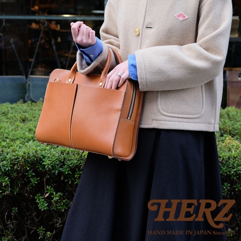 職人手作皮革雙口袋兩用商務公事包，棕色皮革，方形包身，頂部有提把，正面有兩個外口袋，側邊有拉鍊開口，包底有金屬腳釘。