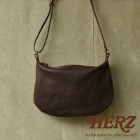 深棕色皮革製成的單肩半月包，包身柔軟，有拉鍊開合，附有可調節長度的皮革肩帶，簡約設計，適合日常攜帶。