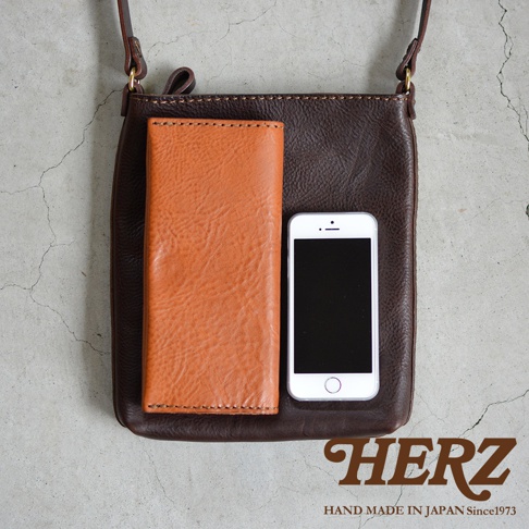 職人手作皮革Organ肩背小方包，深棕色牛皮材質，包包內放置一個橘棕色長夾和一支白色手機。
