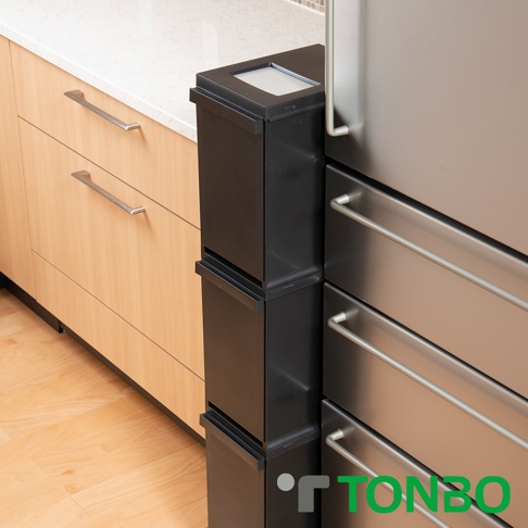 黑色三層抽屜式分類垃圾桶，具備銀色抽屜把手，與木紋櫥櫃和不銹鋼冰箱並列於廚房檯面下。