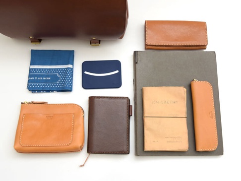 職人手作皮革雙扣兩用側背包 (CW-137) S，包含一個較大的棕色皮革包，下方有藍色印花手帕、藍色卡夾、棕色錢包、深棕色筆記本、卡其色文件夾、卡其色鉛筆筆袋，以及一個棕色長形錢包。