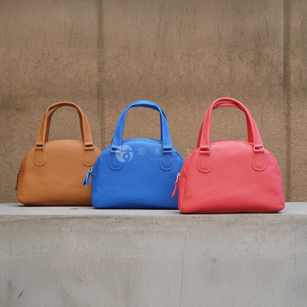 三款京都職人手作半月迷你手提包，分別為焦糖棕、亮藍與珊瑚紅，皆為荔枝紋皮革材質，設計簡約，配有提把與拉鍊開口。