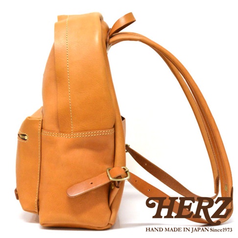 職人手作皮革休閒風後背包 R-93，採用駱駝色皮革製成，側邊可見拉鍊口袋、皮帶扣調整帶及寬版雙肩帶，縫線清晰，展現自然皮革紋理。