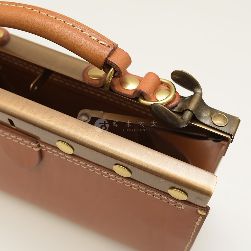 職人手作皮革復古口金兩用手提包，採用棕色皮革，搭配古銅色金屬口金與提把扣環，車縫線清晰，質感細膩。