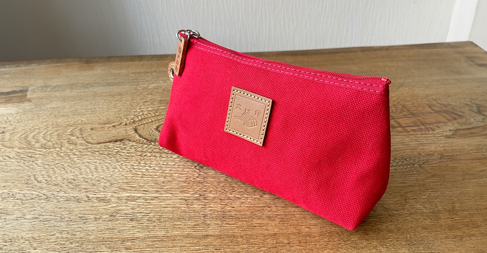 紅色石洗帆布製成的小型收納包，配有拉鍊和皮革標籤，標籤上印有圖案。