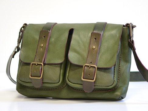 綠色皮革雙口袋肩背包，帶有兩個翻蓋，每個翻蓋都配有皮帶和金屬扣。包包有深色皮革飾邊和肩帶，並採用手工縫線。