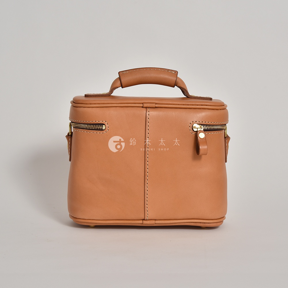 職人手作皮革軟皮相機包，淺棕色，方形立體設計，頂部有提把，兩側有拉鍊隔層，材質柔軟，車縫線明顯。